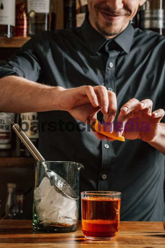 Bartender Garnishing Boulevardier on a Wood Bar Top