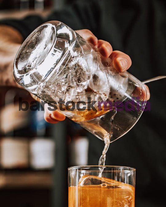 Stirred Cocktail Being Poured Over Clear Ice II